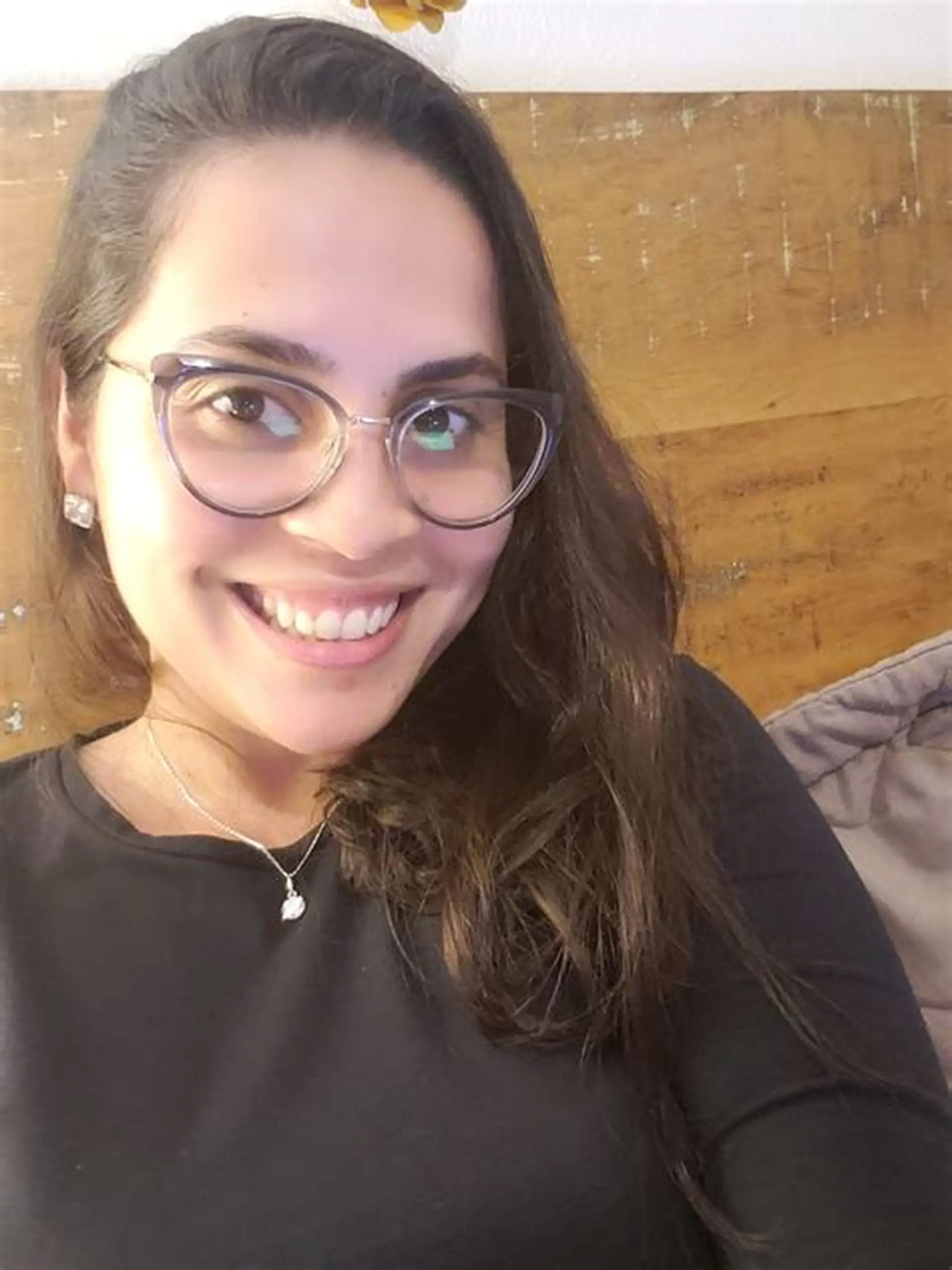 Mulher sorridente de cabelos castanhos longos e óculos, usando blusa preta e colar de prata.
