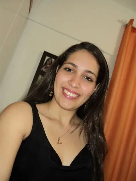 Mulher sorridente com longos cabelos escuros, vestindo uma blusa preta e um colar dourado.